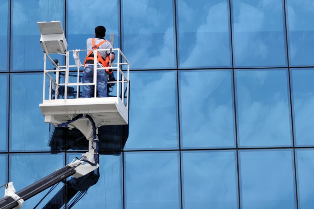 Technician on an aerial lift cleaning a glass building facade